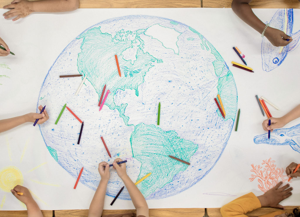 A group of young children working on a giant crayon doodle of the globe