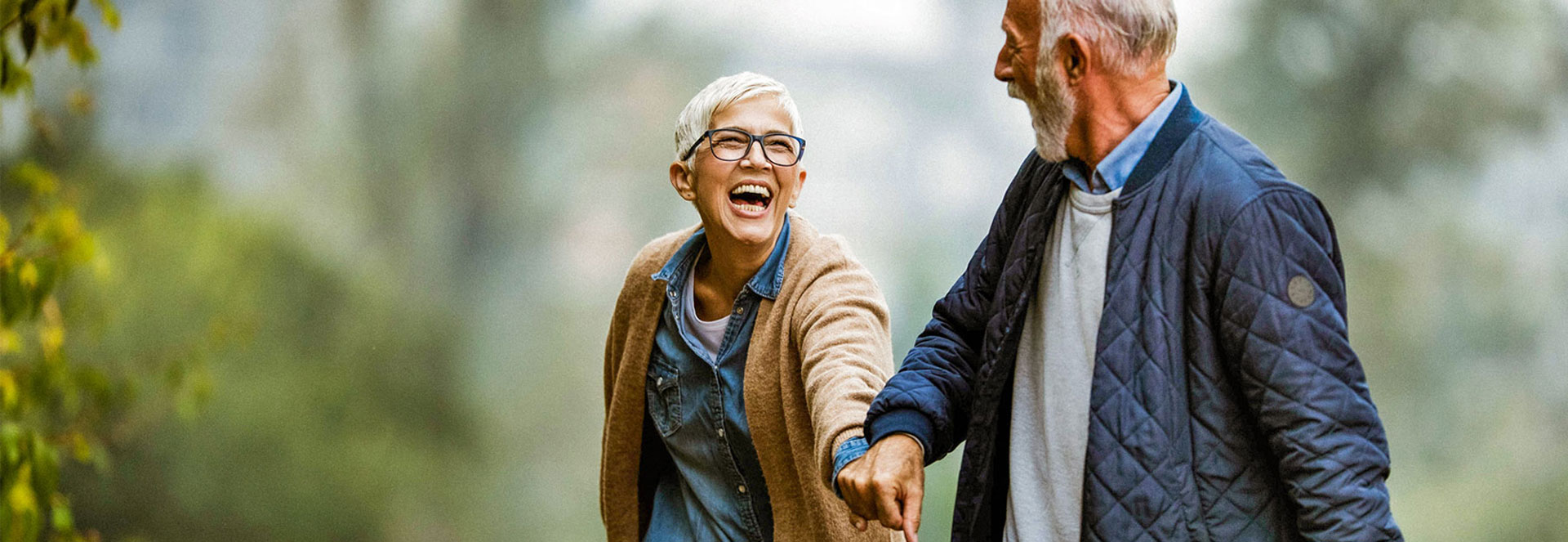 A senior couple is having fun and smiling as they walk thru a lush green park