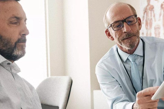 A patient in a doctor's office looks at a tablet a doctor is holding while the doctor explains what he is seeing.