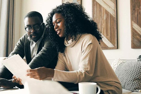 A couple sitting on the couch in their living room reviewing documents related to their investments.