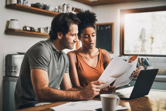 Man and woman seated at a kitchen table looking at retirement contributions on a laptop computer