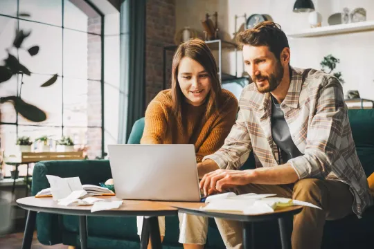 Man and woman seated on a couch looking at investment terms on a laptop computer