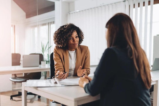 Two women sitting across from one another at a desk.