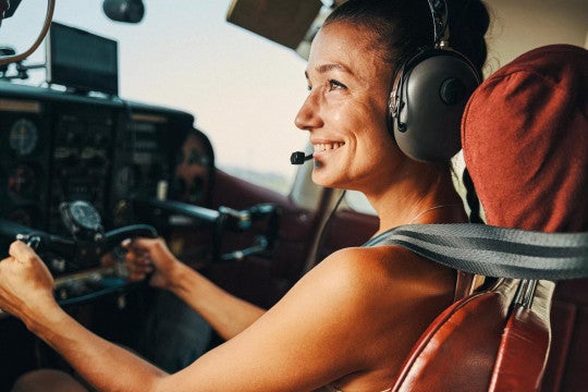 Woman piloting a small aircraft wearing a headset and big smile.