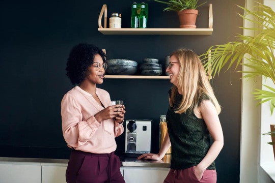 Two employees chatting near office espresso machine.
