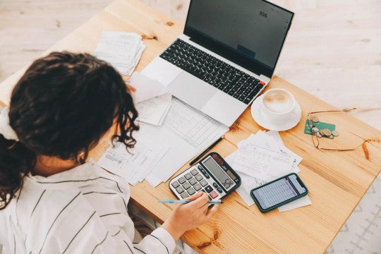 Woman working on taxes and retirement planning using calculator and notebook.