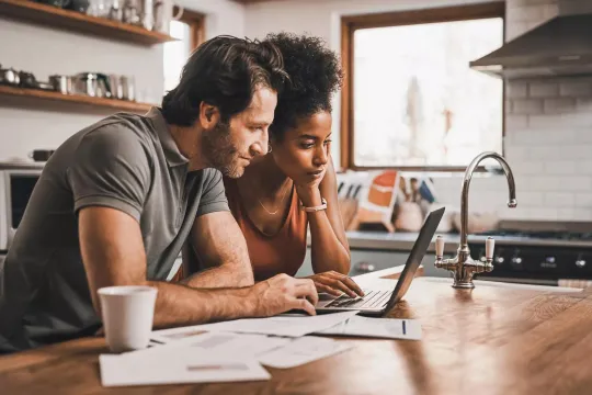 Couple in their kitchen doing financial planning on a laptop.