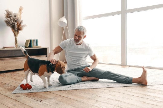 Man sitting on floor, stretching, while petting his dog.
