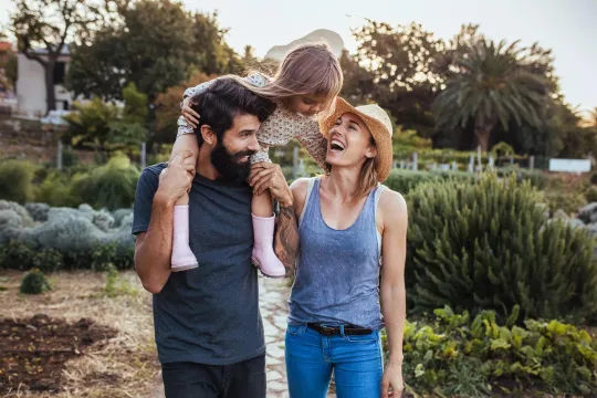 Millennial man and woman walking in nature with child on man's shoulders.