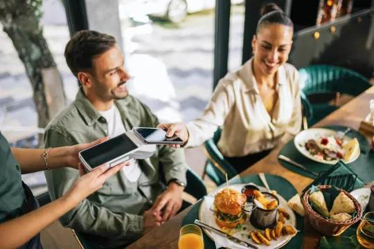 Mujer paga su comida con el teléfono móvil mientras sale a comer con amigos.