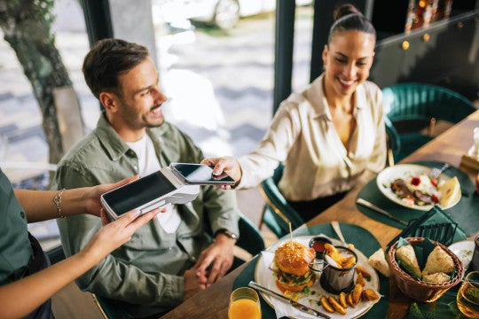 Mujer paga su comida con el teléfono móvil mientras sale a comer con amigos.