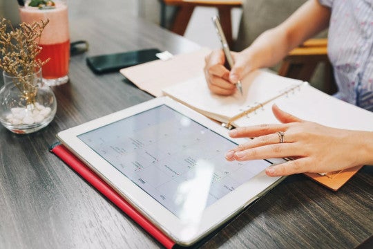 Person adding financial dates to paper calendar and computer calendar.