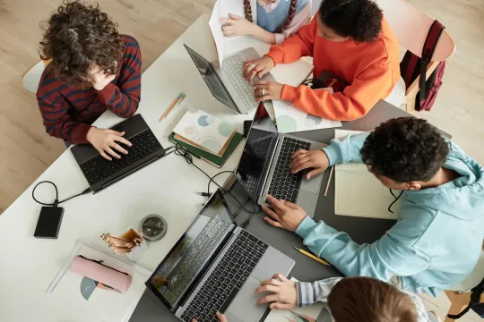 Students gathered around a table working on laptops.