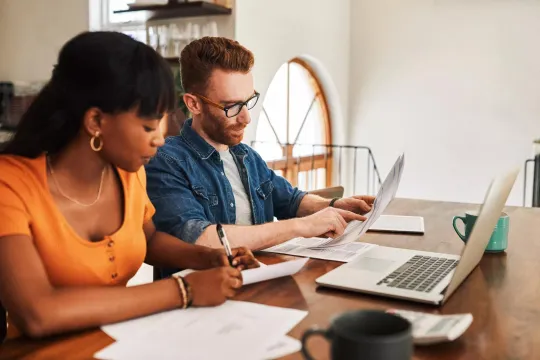 Couple looking at paperwork while sitting with their laptop.