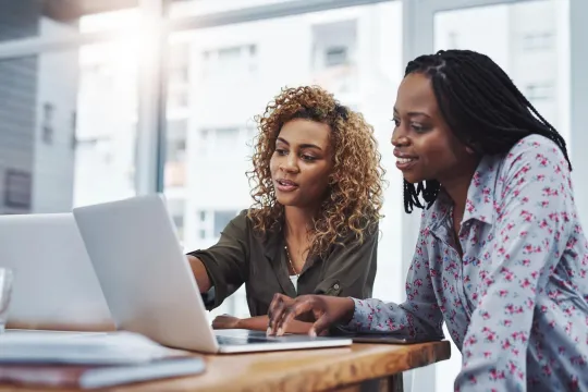Two Black women reviewing financial information on computers.