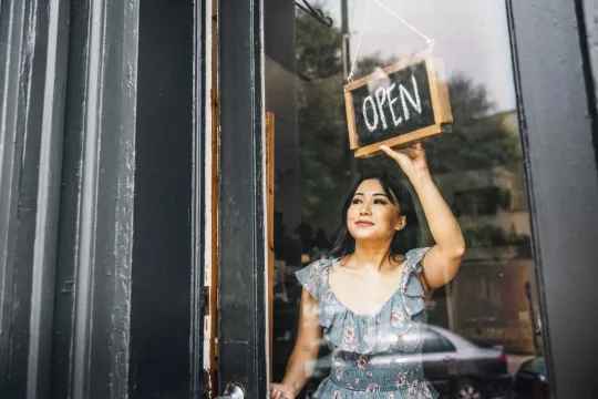 A woman turning the open sign on the front door of a small business.