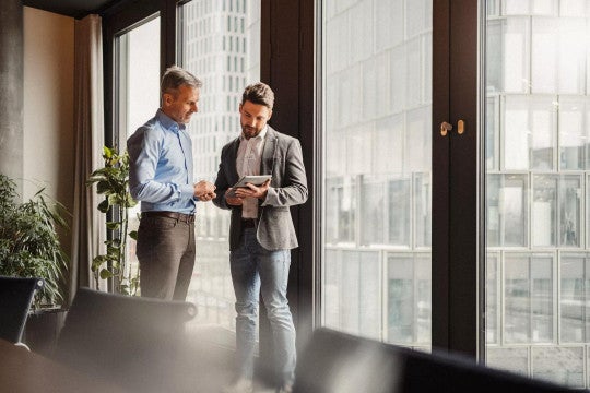 Two men standing in a conference room looking at a tablet computer.