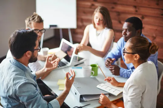 Five employees around a table discussing workplace benefits.
