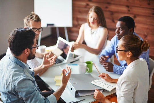 Five employees around a table discussing workplace benefits.