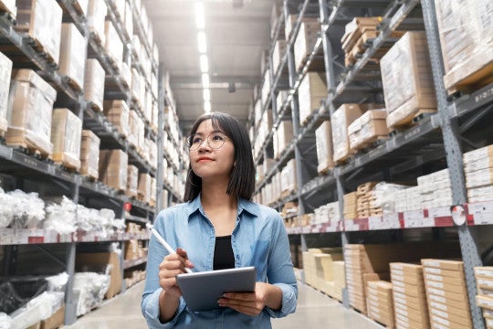 A woman taking inventory in a large aisle of supplies and products.