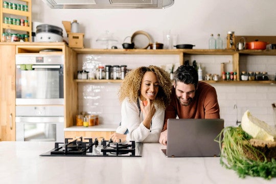 Man & woman in kitchen looking at financial information on a laptop