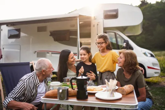 Grandparents, mom, and two daughters eating at table outside with RV in background