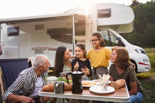 Grandparents, mom, and two daughters eating at table outside with RV in background