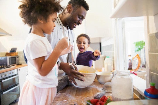 Family baking together in kitchen - adult and two children mixing ingredients in bowls on counter 