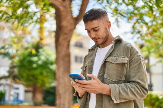 Man in an outdoor setting looking at his cell phone.