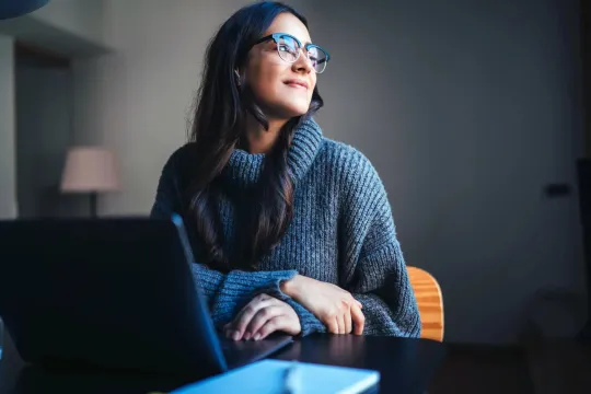 A woman seated behind a laptop in a home office.