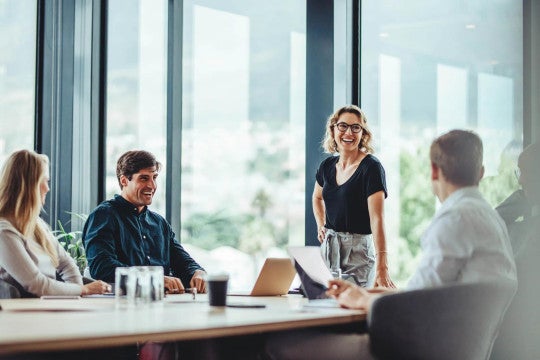 our employees, one of whom is standing, around a desk smiling and discussing business.