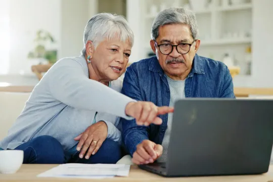 A man and woman looking at a laptop in their home.
