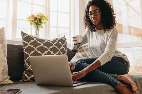 Woman sitting on couch holding coffee cup looking at her computer