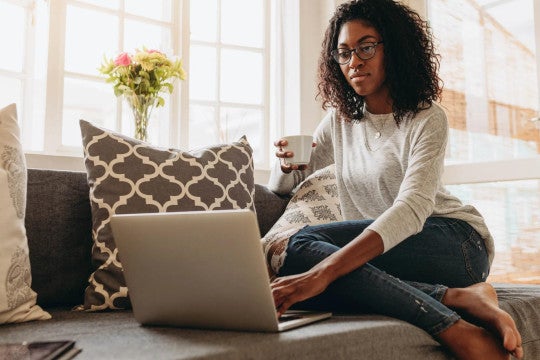 Woman sitting on couch holding coffee cup looking at her computer