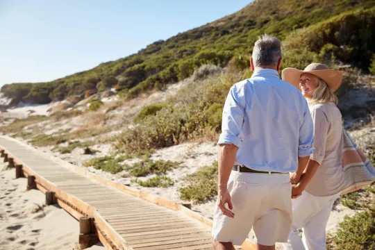 Older couple walking on sidewalk on beach.