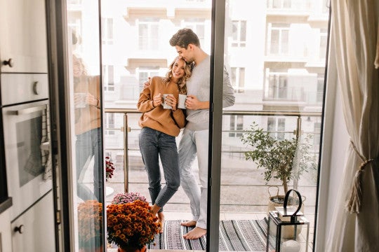 Man and woman standing in the sunlit kitchen happily with coffee mugs