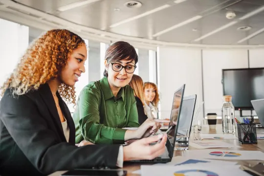 Two women sitting next to each other looking at a computer screen.