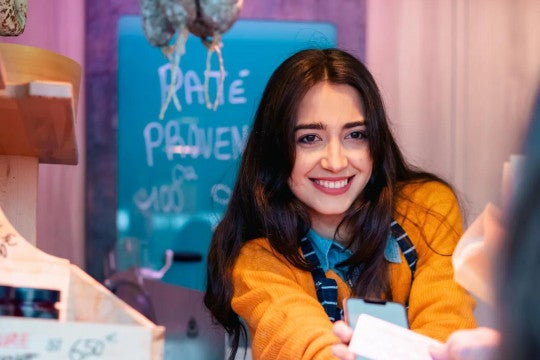 A young woman behind the counter at a butcher shop receives a digital payment from a customer. 