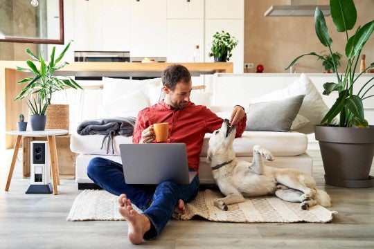 Man, sitting on floor looking at computer, with his dog