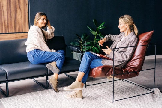 Two women seated in office space having a conversation.