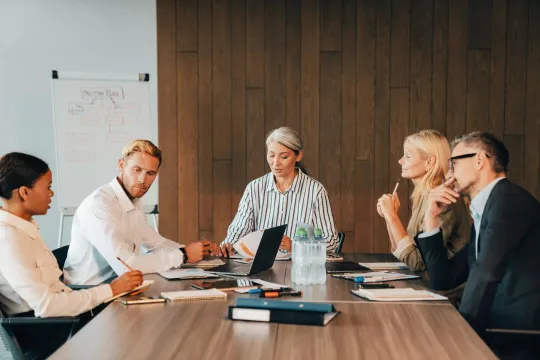 Six professionals seated at a conference table reviewing documents during a meeting.