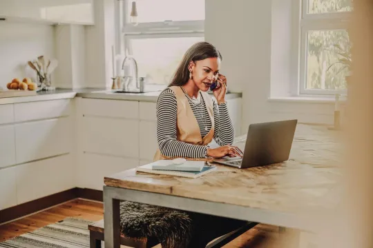 Woman at home working on computer and talking on cellphone.
