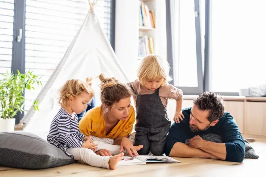 Madre y padre jóvnes leyendo a sus hijos en su sala de estar.