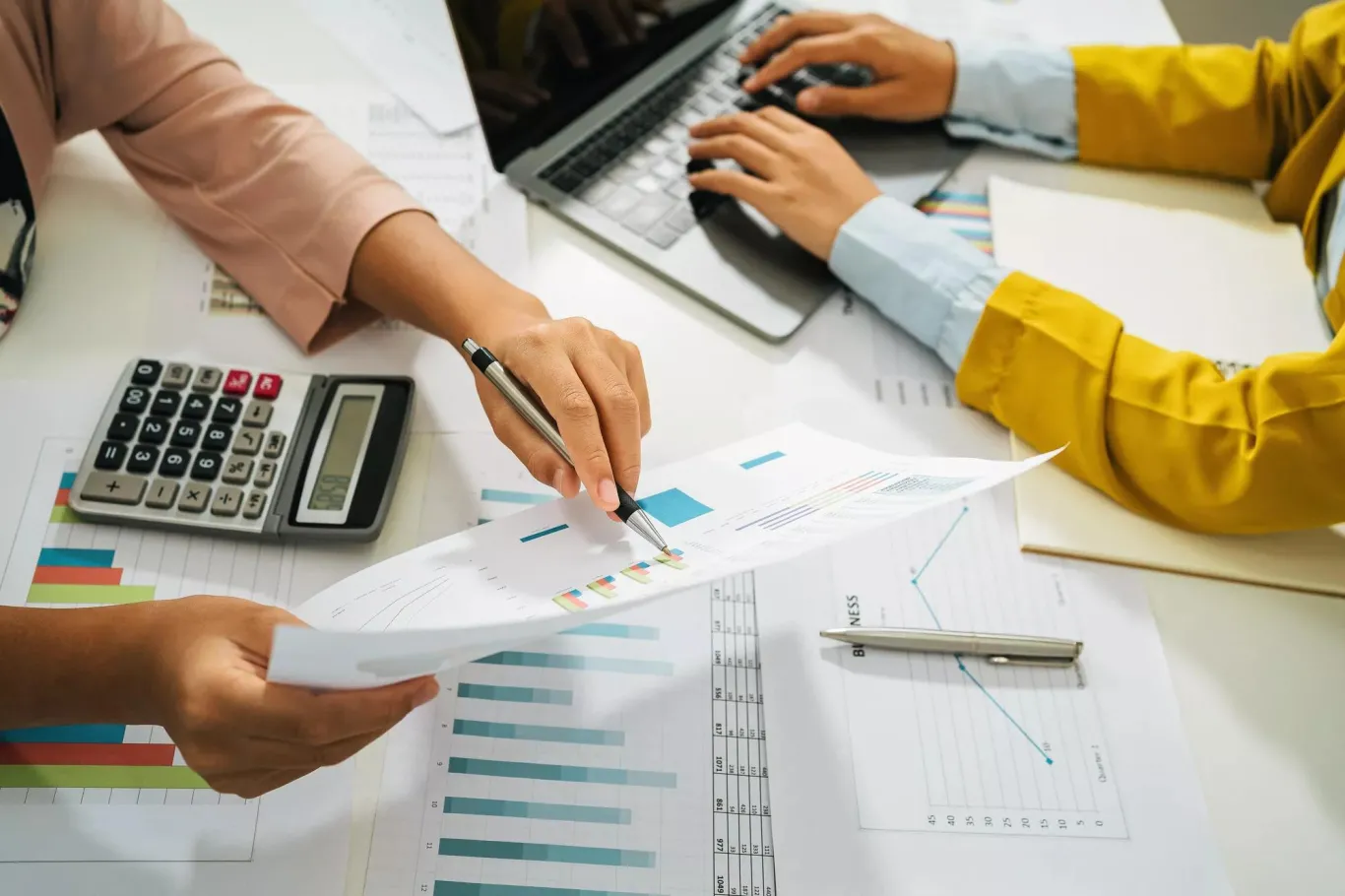 Two business colleagues comparing data using a calculator and laptop.