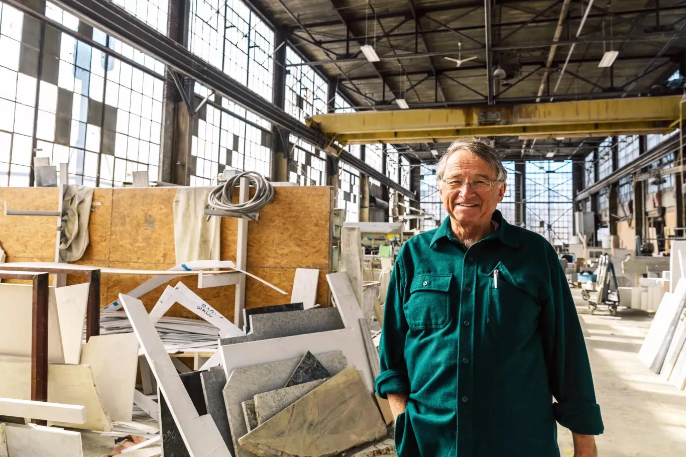 ESOP business owner of fabrication shop wearing green coveralls standing in front of the manufacturing production floor.