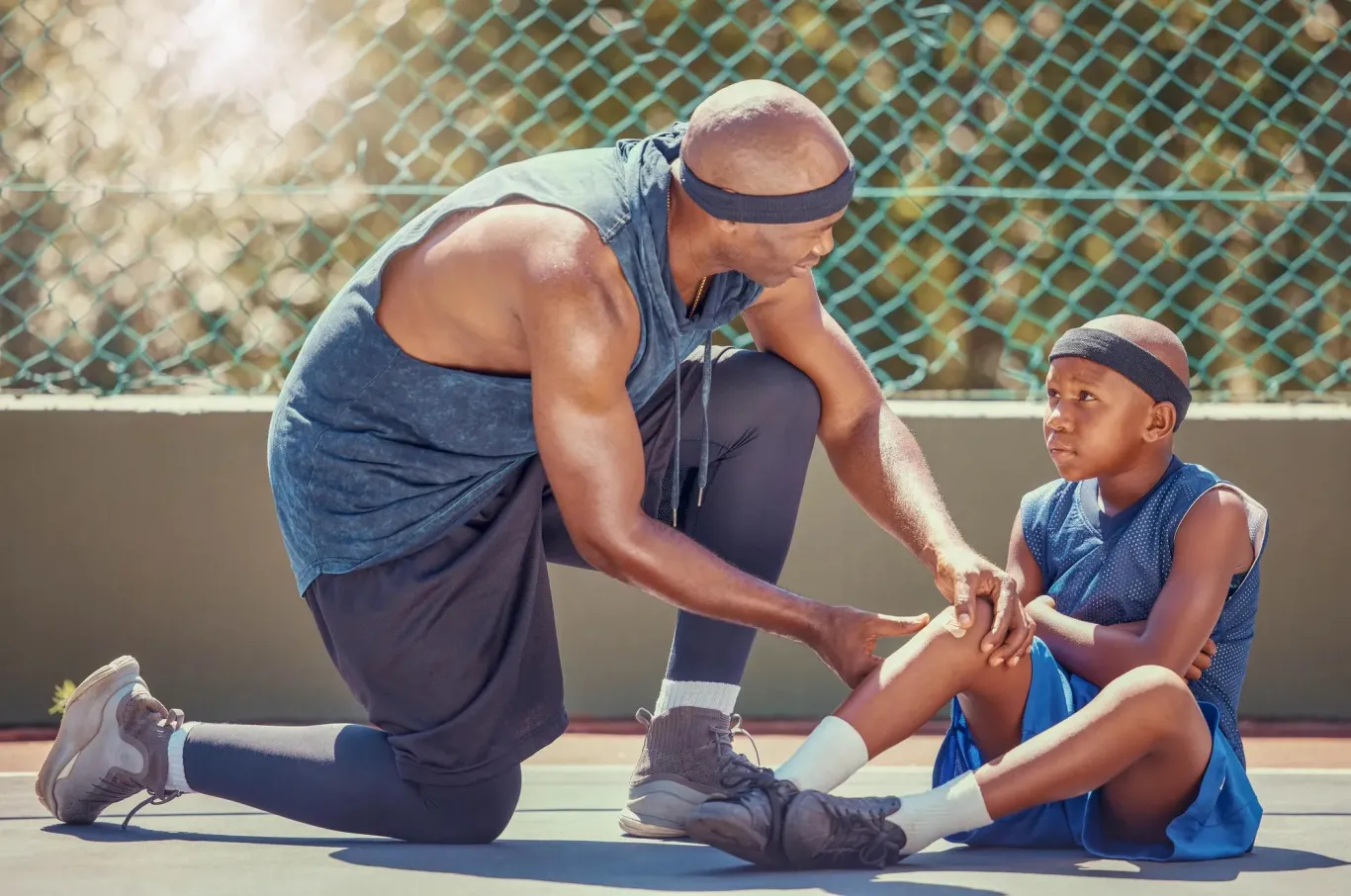 A child sitting on the ground with a potentially injured leg with an adult examining the child's leg.