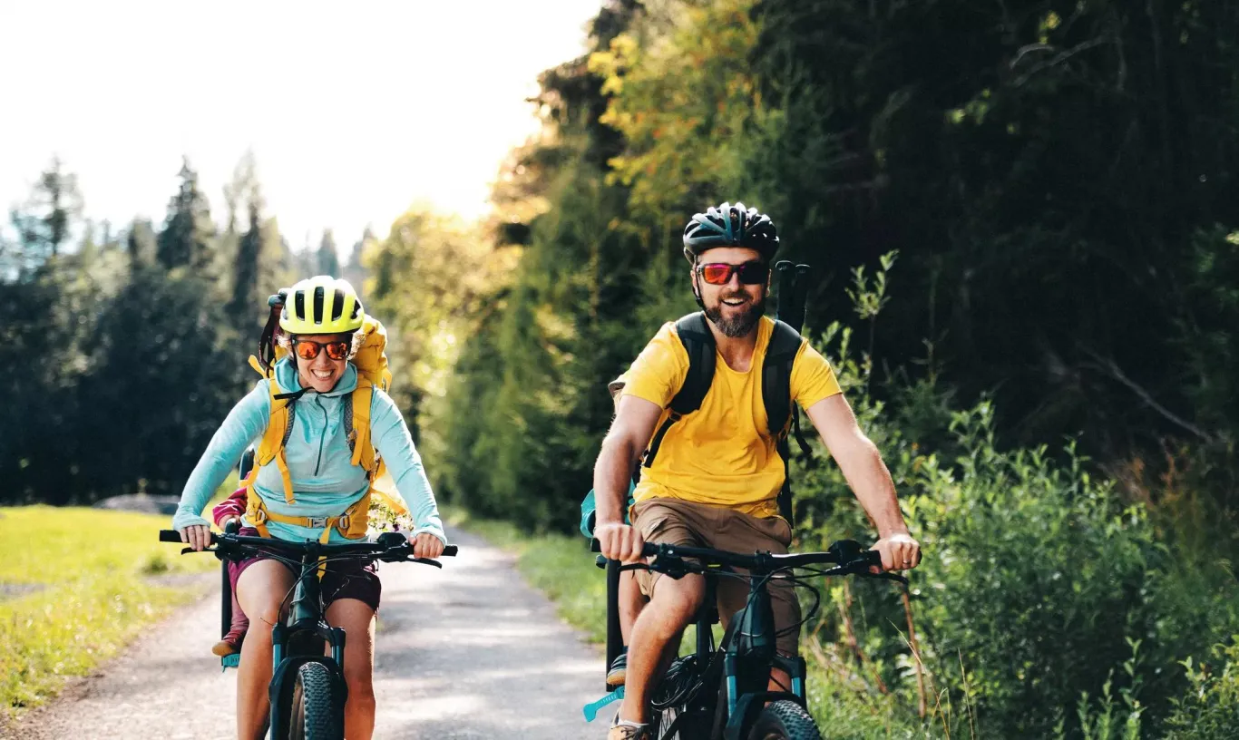 A family of bikers riding along a bike trail surrounded by green trees.