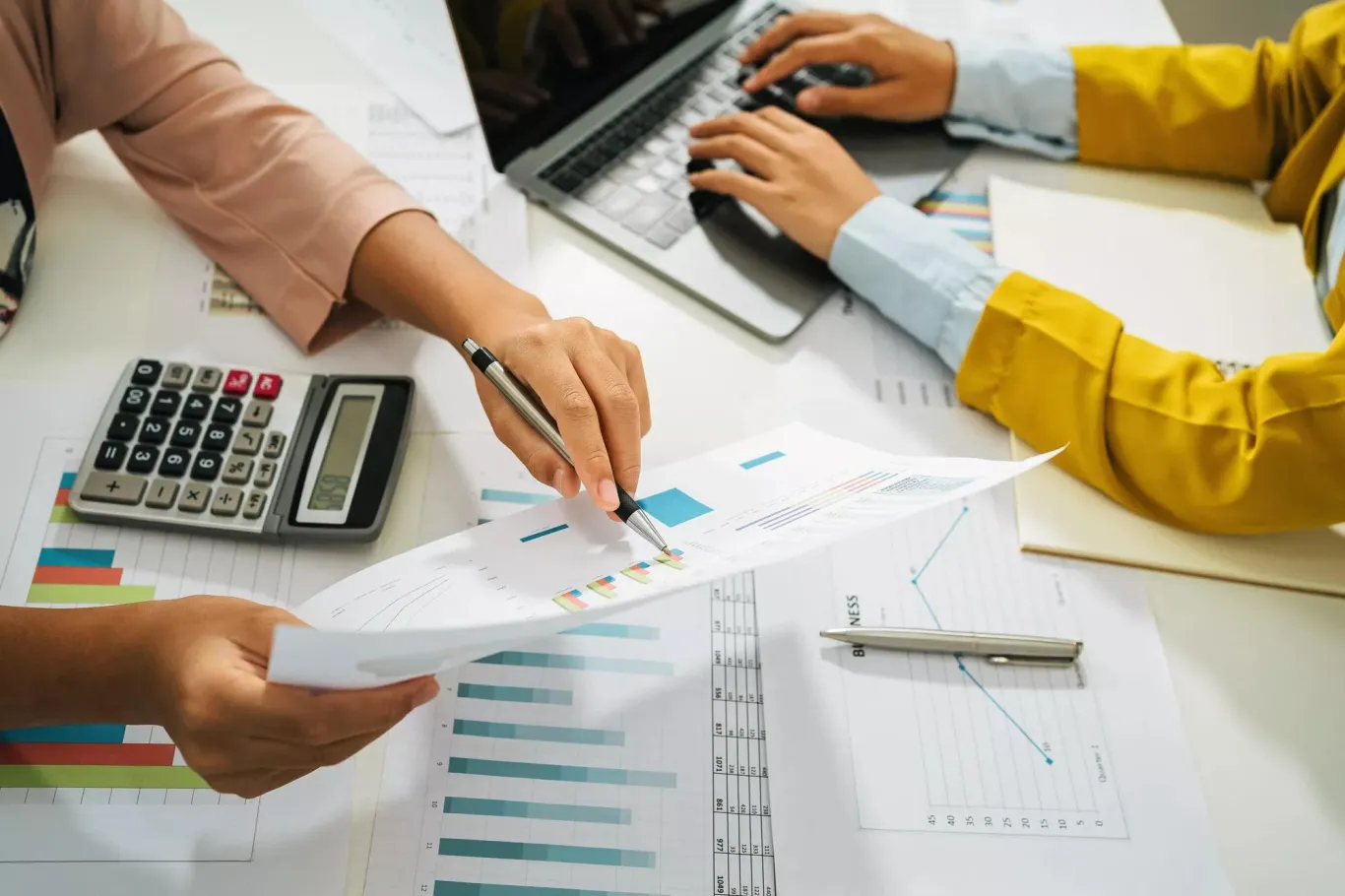 Two business colleagues comparing data using a calculator and laptop.