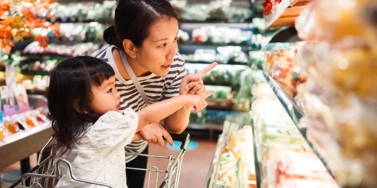 Mother and her toddler-aged daughter shop the produce section of the grocery store.