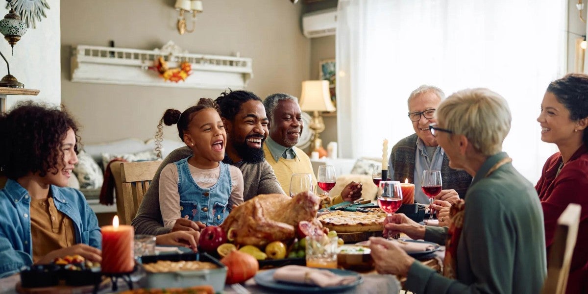 A happy family representing at least three generations sits around the dinner table to share a meal.